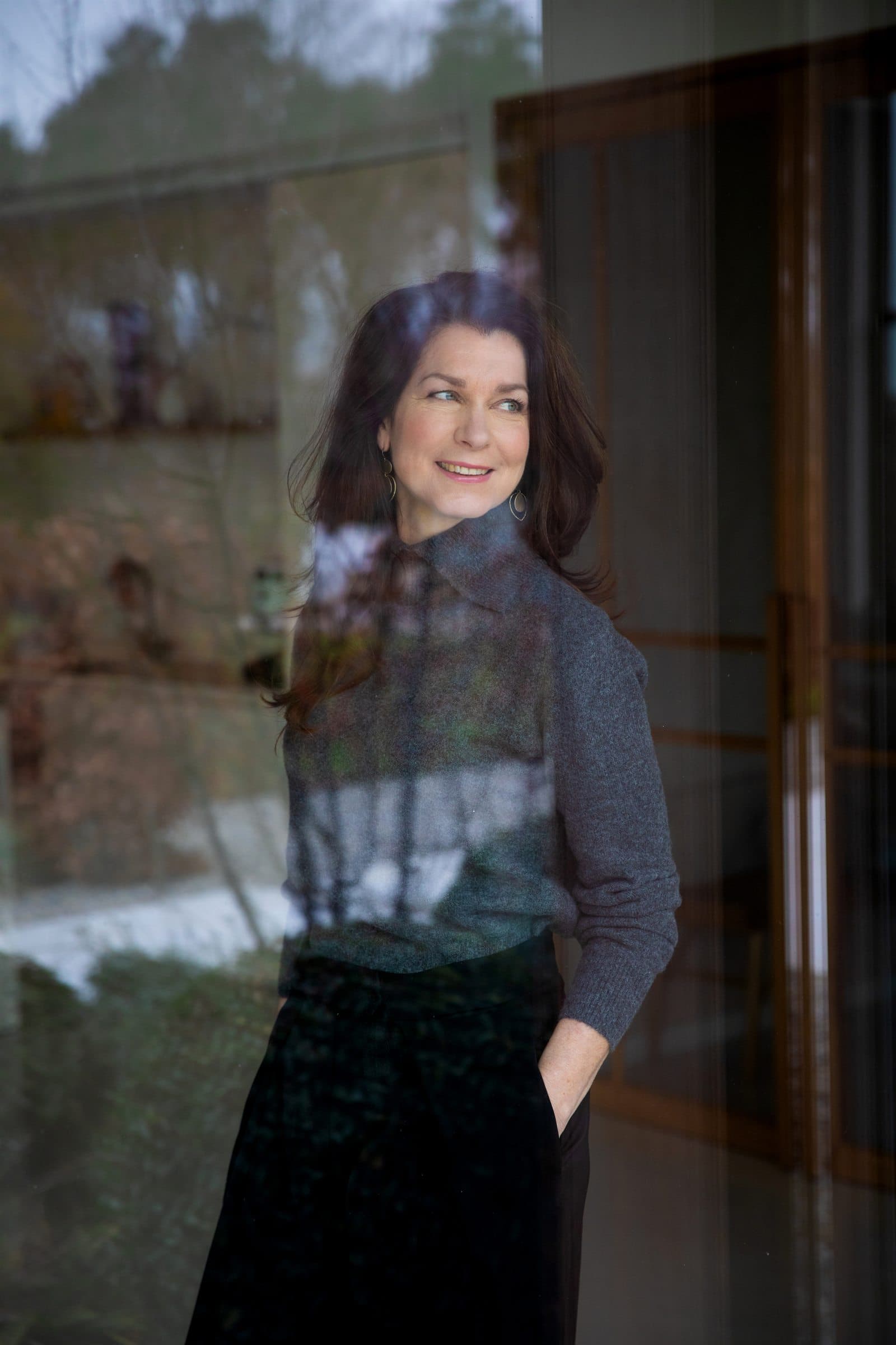 Mariska de Kleijne achter glas, met de weerspiegeling van de omgeving over haar portret