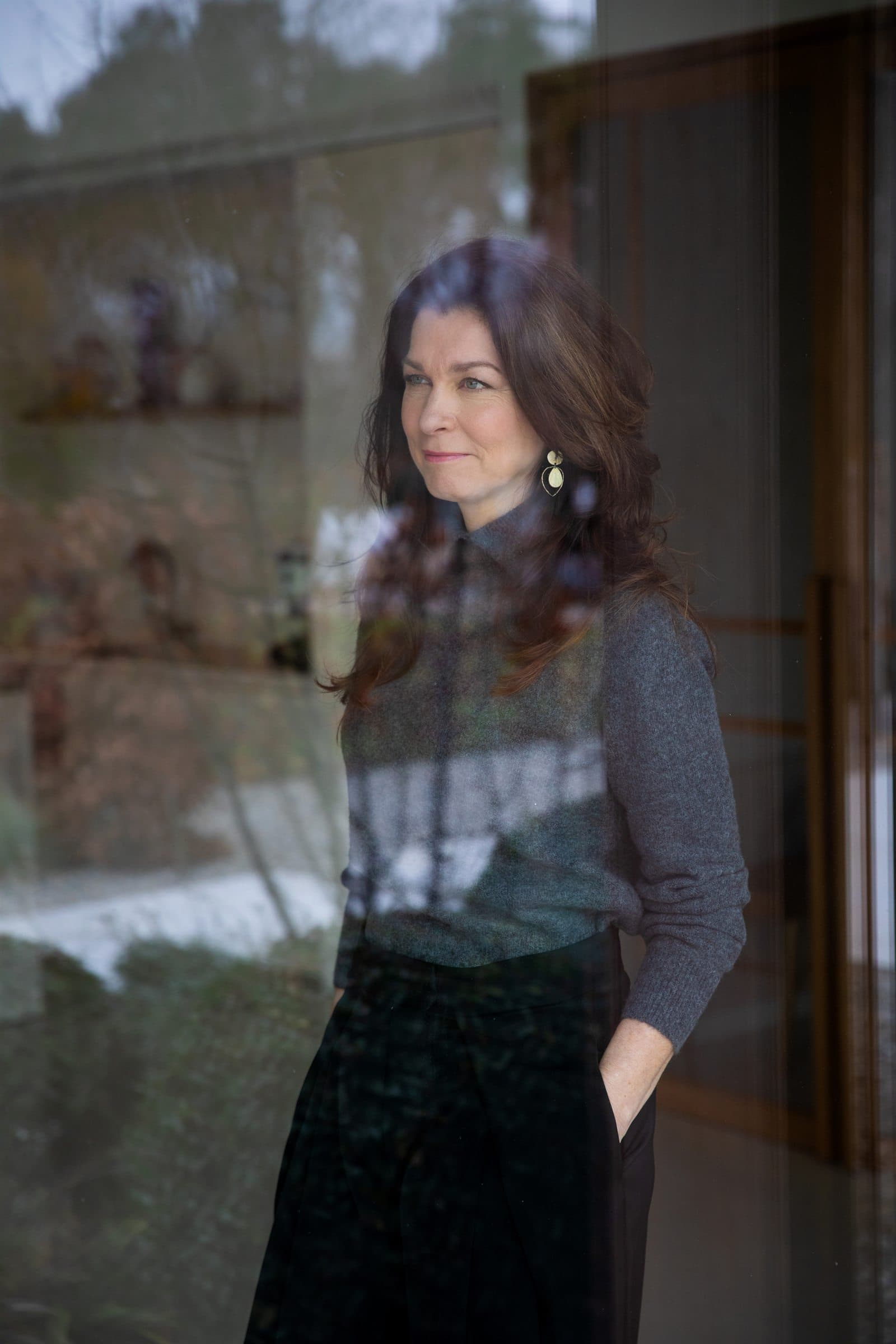 Mariska de Kleijne bij een glazen wand, met de omgeving weerspiegeld in het glas